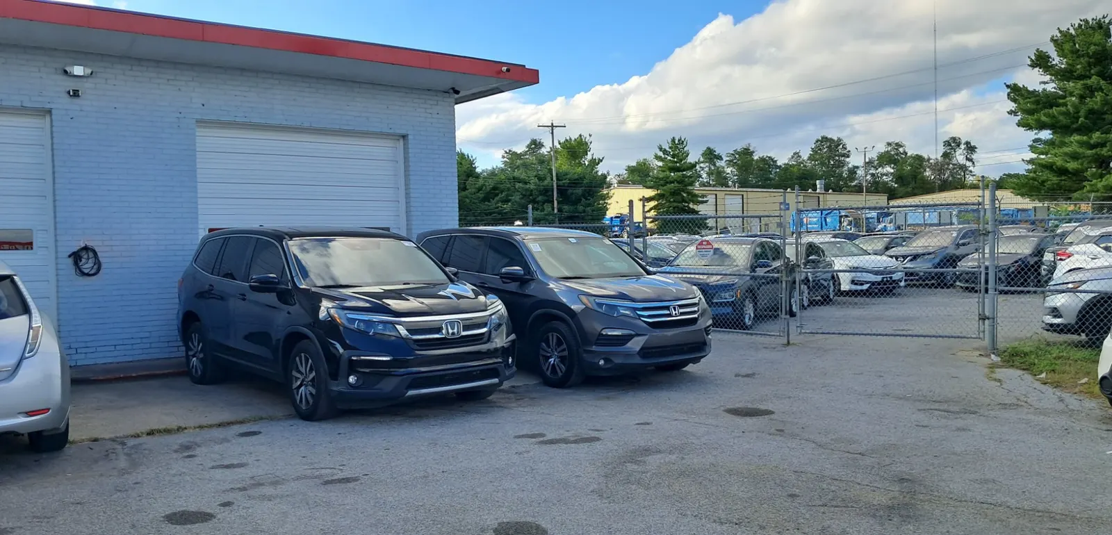 Two SUVs beside the service bay with a fenced yard of vehicles behind them.