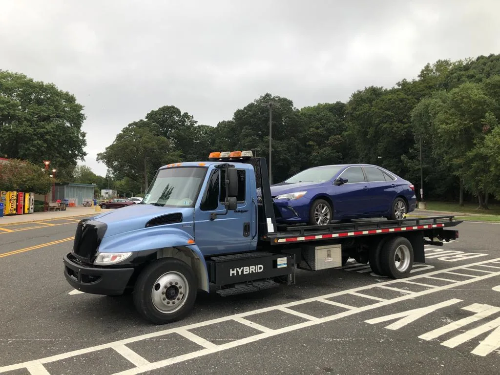 A blue flatbed tow truck carrying a blue passenger car.