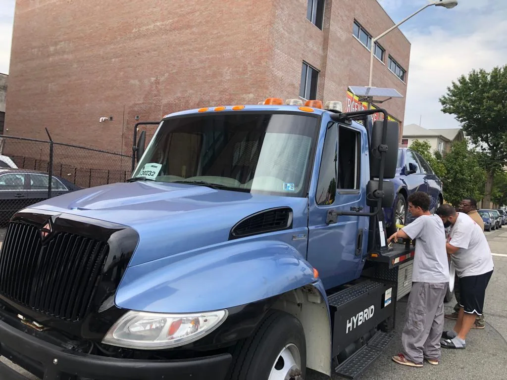Three people loading a passenger car onto the blue flatbed tow truck.