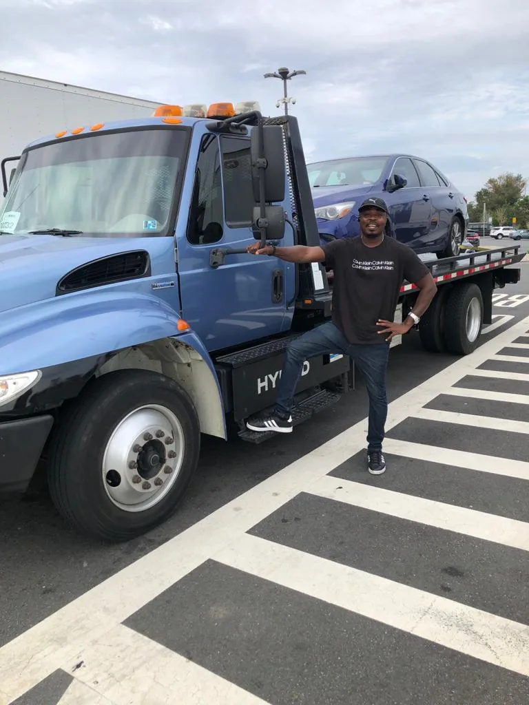 A CM Towing operator standing beside the blue flatbed truck and a passenger car.
